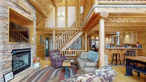 A log cabin interior with a stone fireplace, wooden staircase, and a dining area. - Rustic 4BR Cabin - HOT TUB - McHenry (McHenry)