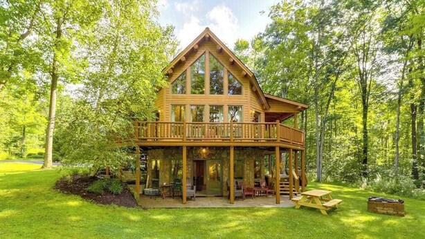 A wooden cabin with a balcony, surrounded by a lush green forest. - Rustic 4BR Cabin - HOT TUB - McHenry (McHenry)