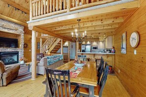 A wooden interior with a dining area, fireplace, kitchen, and staircase. - Rustic 4BR Cabin - HOT TUB - McHenry (McHenry)