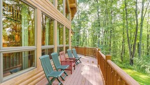 A wooden deck with large windows and chairs, surrounded by a forest. - Rustic 4BR Cabin - HOT TUB - McHenry (McHenry)