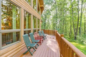 A wooden deck with large windows and chairs, surrounded by a forest. - Rustic 4BR Cabin - HOT TUB - McHenry (McHenry)