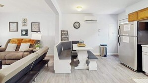 Un salon moderne comprenant un canapé, un banc, une table à manger et un coin cuisine avec un réfrigérateur.
