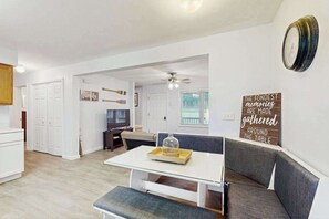 A modern kitchen with white cabinets, a dining table with a glass top, and a seating area with a bench and a sofa. - 3BR - Wooded Retreat - Fire Pit (Oakland)