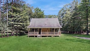 Une maison de plain-pied avec un porche, entourée d’une pelouse bien entretenue et d’arbres.