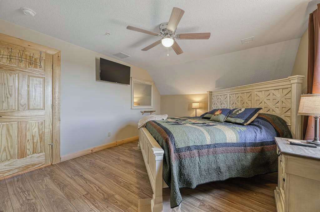 Ein Schlafzimmer mit Bett, Holzschrank, Deckenventilator und einem an der Wand montierten Fernseher.