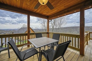 A covered deck with a table and chairs, overlooking a landscape with hills and a house.
