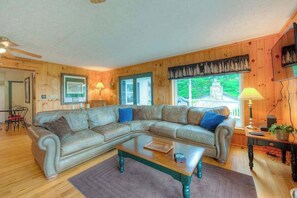A wooden-paneled living room with a sectional sofa, a coffee table, and a view of a building through a window.