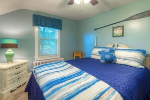 A bedroom with a bed, a nightstand, a lamp, a window with blinds, and a ceiling fan.