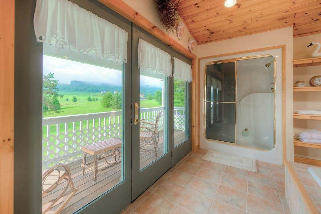 A covered outdoor area with a bench, a glass-enclosed shower, and a view of a green landscape.