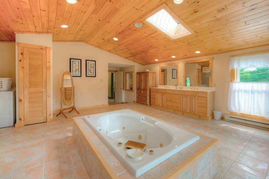 Ein geräumiges Badezimmer mit einer großen Badewanne, Holzboden und einem Oberlicht.