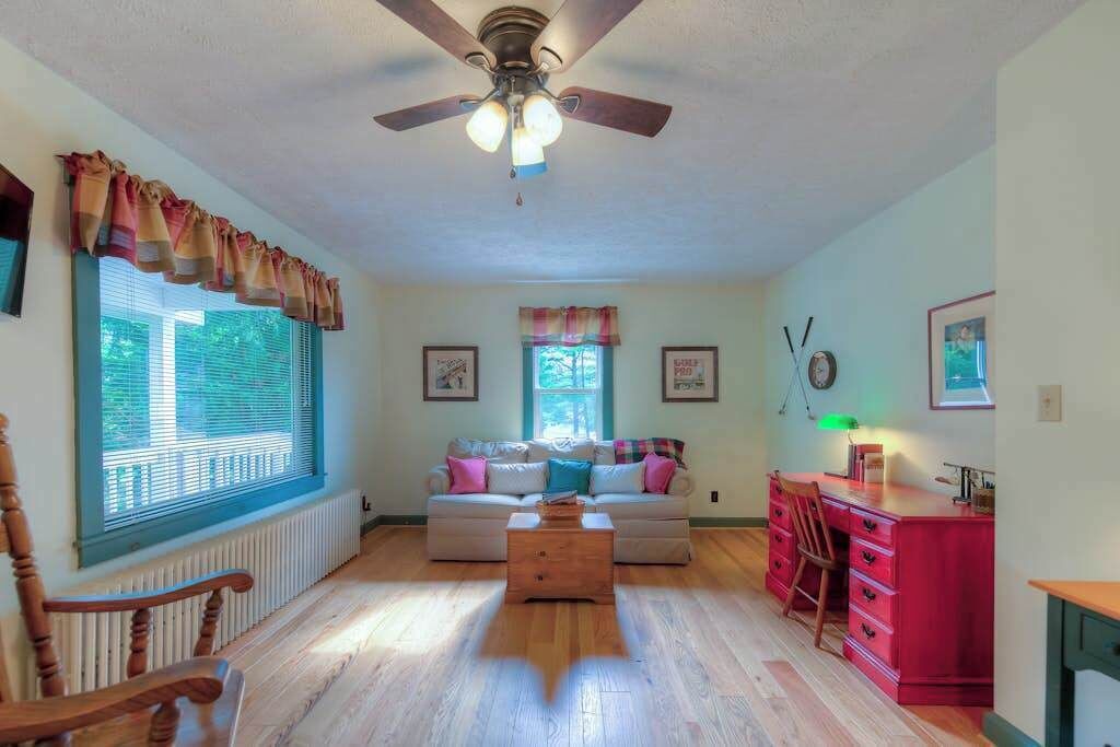 A living room with a ceiling fan, a sofa, a coffee table, a desk with drawers, and a chair.