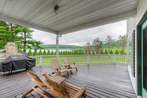 Una terraza techada con sillas Adirondack, una parrilla y vistas a un paisaje verde.