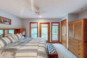 Una camera da letto con un letto, una ventola a soffitto, un armadio in legno e ampie finestre.