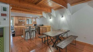 Uma cozinha rústica com armários de madeira, uma mesa de jantar e um teto alto com vigas aparentes.