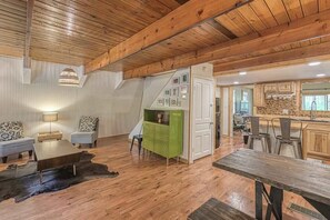 Un intérieur rustique avec des poutres en bois, un coin repas, une cuisine et un espace de vie comprenant un canapé et une lampe.