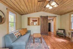 Une pièce avec un plafond en bois, un canapé bleu orné de coussins à motifs, une petite table en bois et une chaise verte.