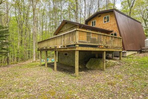 Una cabaña de troncos con terraza, rodeada de bosque.