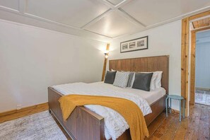 Quarto com cama de madeira, mesa de cabeceira, abajur e quadro na parede.