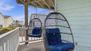 Zwei Hängesessel mit blauen Kissen auf einer Veranda mit Geländer.