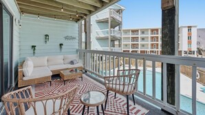 Ein Balkon mit Korbmöbeln, ein Pool und Blick auf benachbarte Gebäude.