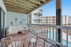 Ein Balkon mit Korbmöbeln, ein Pool und Blick auf benachbarte Gebäude.