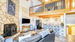 Ein großzügiger Wohnbereich mit Steinwand, Kamin, Fernseher, einem Balkon mit Holzbalkonen und einer Küchenzeile.