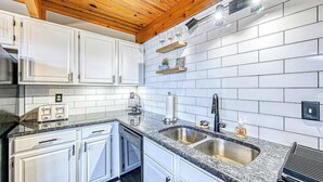 Eine moderne Küche mit weißen Schränken, Granit Arbeitsplatten, einer Spüle und Holzbalken an der Decke.
