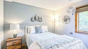 Ein Schlafzimmer mit Bett, Nachttisch, Wandventilatoren und einem Fenster.
