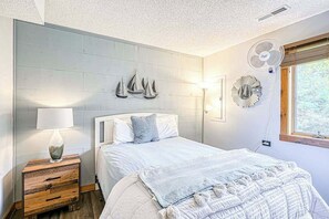 Ein Schlafzimmer mit Bett, Nachttisch, Wandventilatoren und einem Fenster.