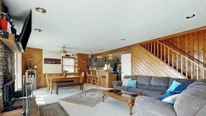 A living room with a fireplace, a sofa, a coffee table, and a dining area with a wooden table and chairs. - Rustic 3BR Cabin - HOT TUB - Oakland (Oakland)