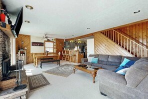 Un salon avec une cheminée, un canapé, une table basse et un coin repas comprenant une table et des chaises en bois.