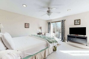Een slaapkamer met een bed, een plafondventilator, een televisie en een raam met gordijnen.