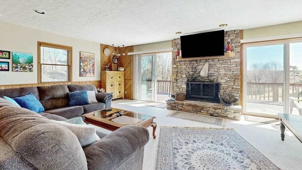 A living room with a stone fireplace, a large flat-screen TV, a sofa, and a coffee table. - Rustic 3BR Cabin - HOT TUB - Oakland (Oakland)