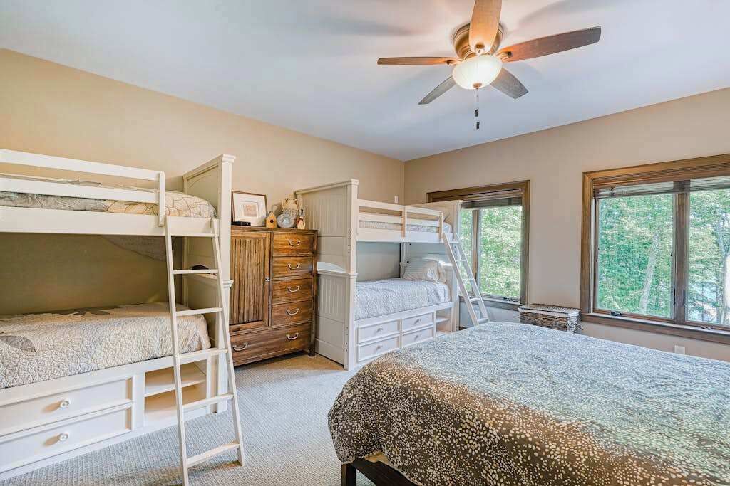 Une chambre avec des lits superposés, un ventilateur de plafond, une commode et de grandes fenêtres.