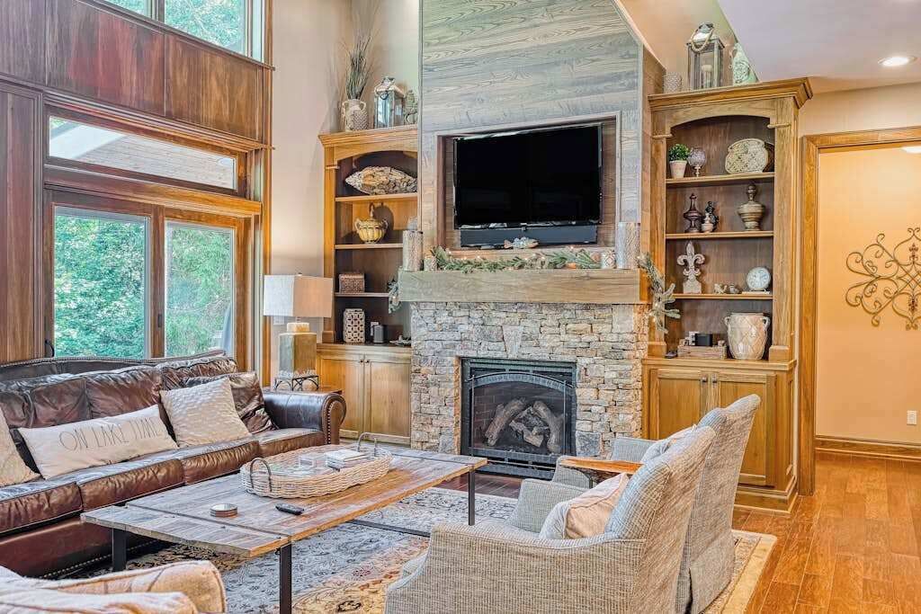 A cozy living room with a stone fireplace, leather sofa, and wicker chairs.