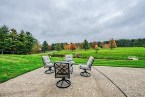 Une terrasse extĂ©rieure avec une table et quatre chaises, un champ dâherbe, des arbres et un ciel nuageux.