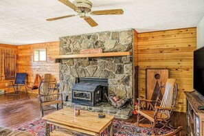 LâintĂ©rieur dâune cabane en rondins, avec une cheminĂ©e en pierre, des murs en bois et un ventilateur de plafond.