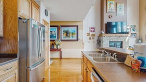 Eine Küche mit Holzausstattung, Edelstahlgeräten, einem Kamin aus Stein und einem Fernseher, der über der Arbeitsfläche angebracht ist.
