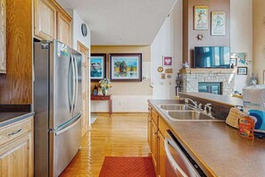 Eine Küche mit Holzausstattung, Edelstahlgeräten, einem Kamin aus Stein und einem Fernseher, der über der Arbeitsfläche angebracht ist.