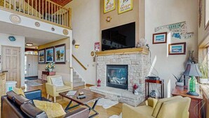 Ein geräumiges Wohnzimmer mit Kamin aus Stein, Ledersofas und einer hohen Decke mit Balkon.