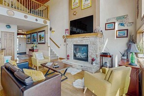 Ein geräumiges Wohnzimmer mit Kamin aus Stein, Ledersofas und einer hohen Decke mit Balkon.