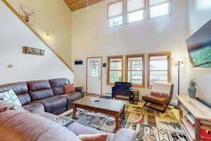 Ein geräumiges Wohnzimmer mit einer Ledersofa, einem Couchtisch und einem Kamin. Große Fenster sorgen für natürliches Licht und einen Blick ins Freie.