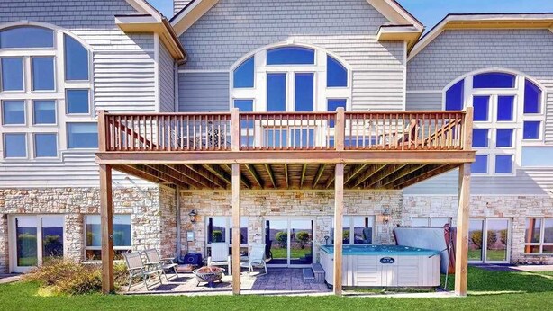 A two-story house with a balcony, a hot tub, and a stone foundation.