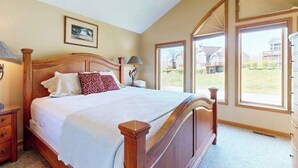 A bedroom with a wooden bed, a nightstand, a lamp, and a window with a view of houses.