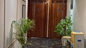 Un vestíbulo de hotel con suelo de mármol, puertas de madera, una planta en maceta, una mesa con sillas y un candelabro en el techo.