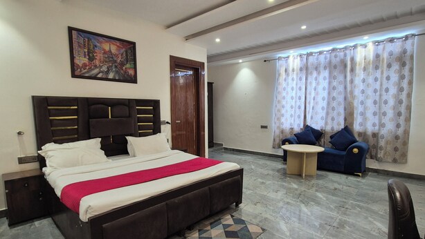 Un dormitorio con cama, cabecera, mesita de noche, escritorio, silla, ventana con cortinas y un cuadro en la pared.