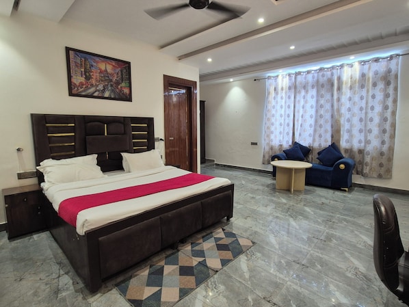 A bedroom with a bed, a headboard, a nightstand, a desk, a chair, a window with curtains, and a painting on the wall. - OnlyStay BnB Golf Course Road (Gurugram)