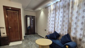 Una habitación con puerta de madera, un armario oscuro, un sofá azul con cojines, una mesa redonda y una cortina estampada.