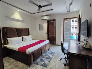 A hotel room with a bed, desk, chair, ceiling fan, air conditioning units, and a view of the outside. - OnlyStay BnB Golf Course Road (Gurugram)
