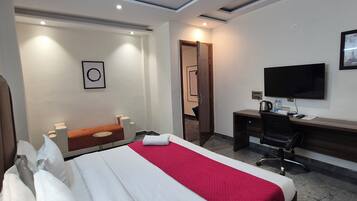 Quarto de hotel com uma cama, escrivaninha, cadeira, televisão e porta.